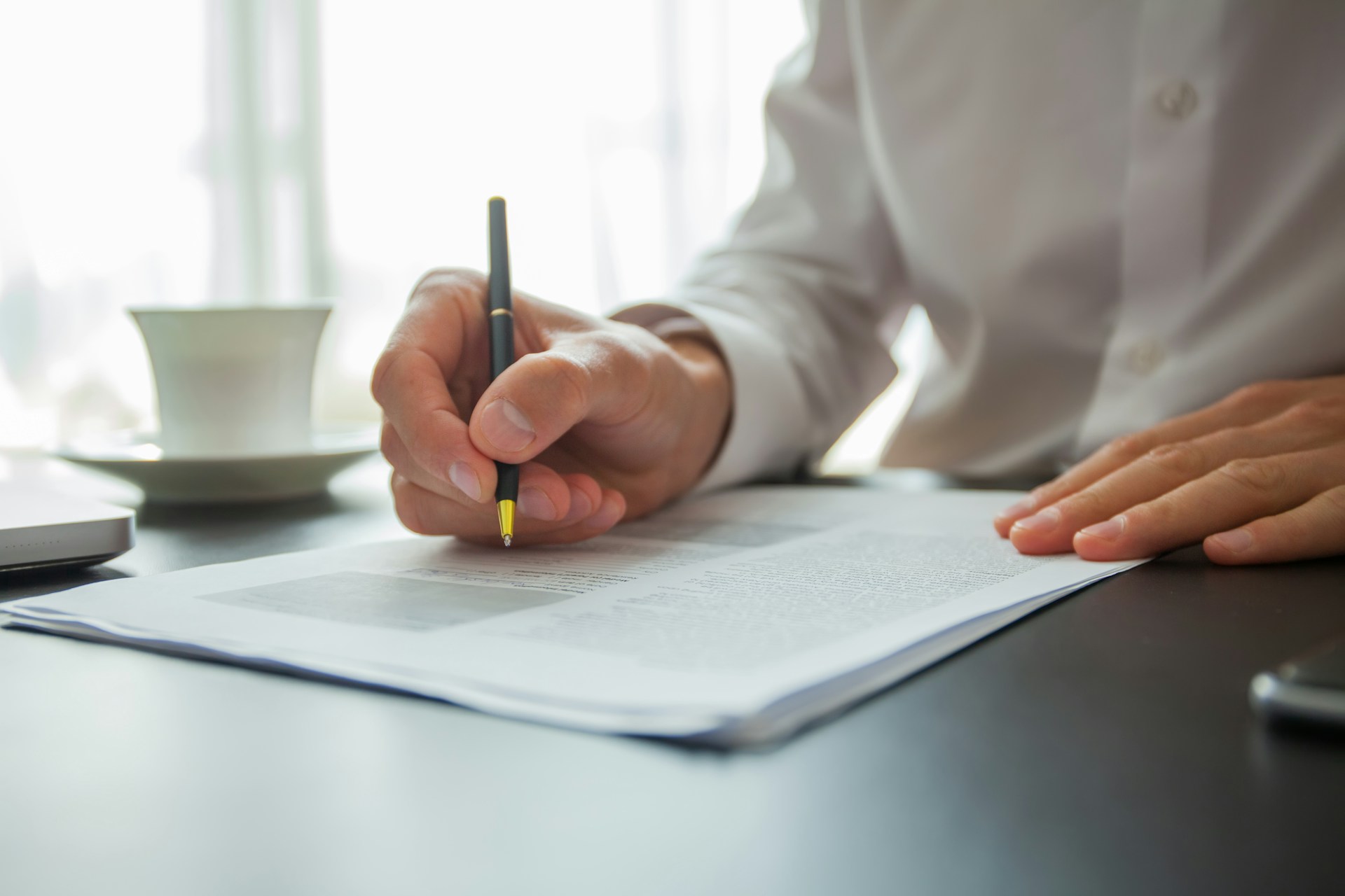 Man signing documents at a table with a cup of coffee beside him