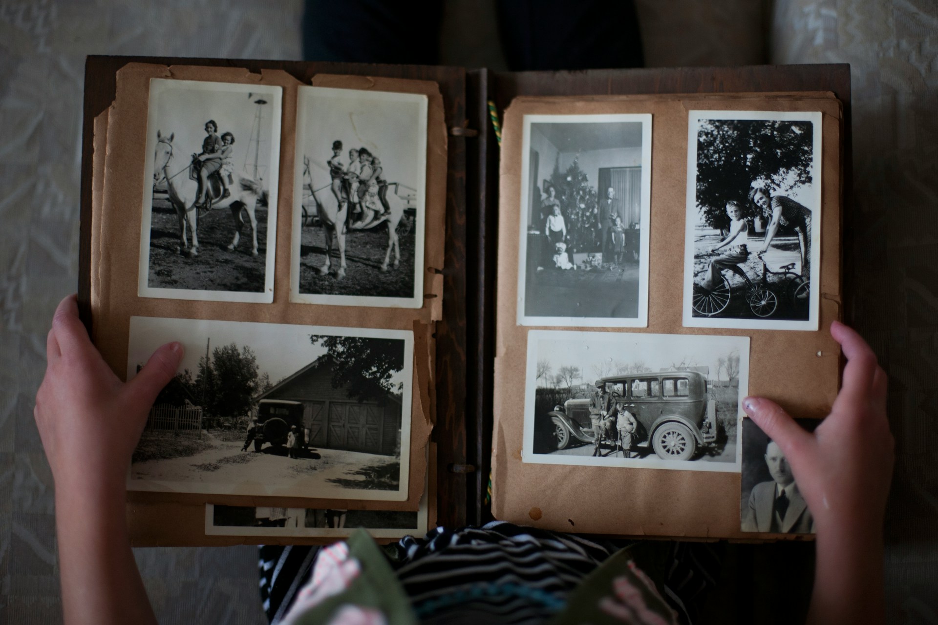 Image of a photo album with six black and white photos of times gone by and two hands holding the book