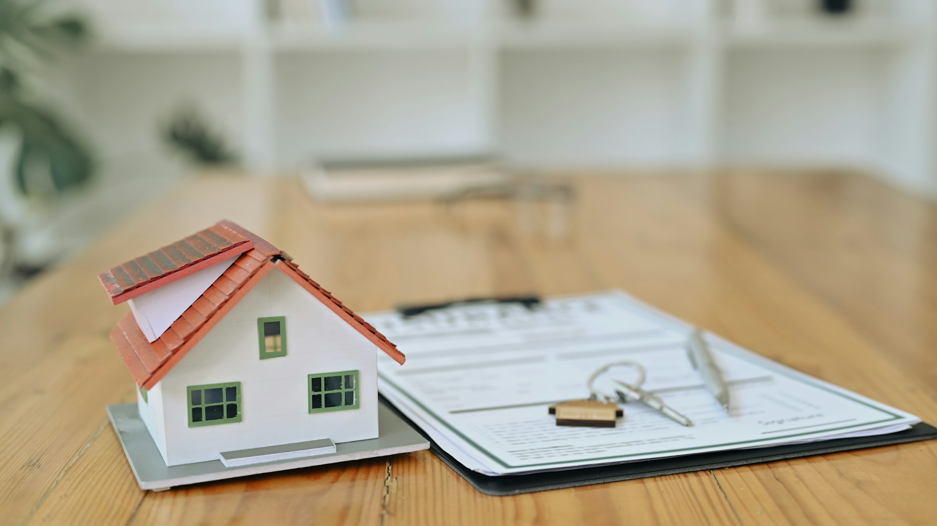 A table with a small toy house and a stack of papers with keys sitting on top.
