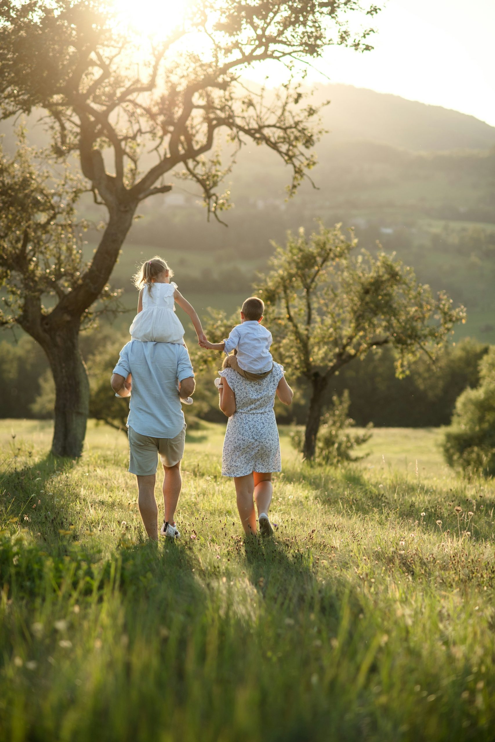 Mother and Father walking in nature each with a child on their shoulders.
