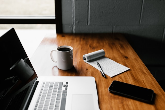 Picture of a desk with a laptop, mug and pad of paper