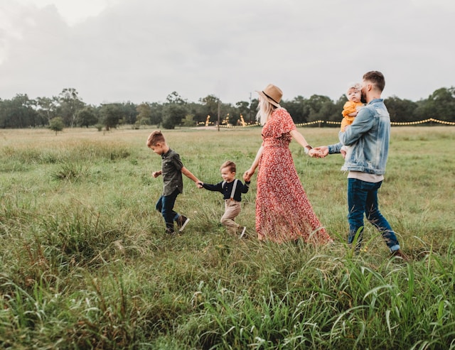 Family of five walking across a field with the oldest son leading and the father in the rear