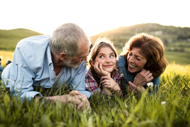 Girl laying in a field between her grandparents laughing