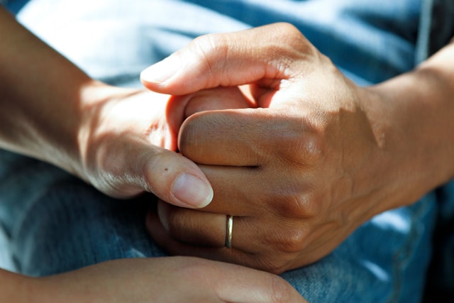 Two hands holding together one a man's the other a woman's on a hospital bed