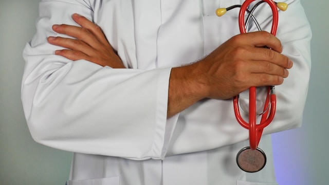 Doctor holding red stethoscope showing only arms in a white doctor's jacket